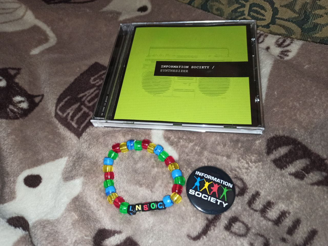 Photo of an Information Society - Synthesizer CD, bracelet that says 'Insoc' and pin that says 'Information Society'